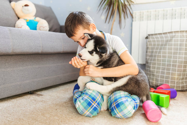 Ein Junge sitzt mit seinem Husky-Welpen auf dem Boden. Kind umarmt seinen Welpen. Tierpflege. Geburtstagsüberraschung - Foto, Bild