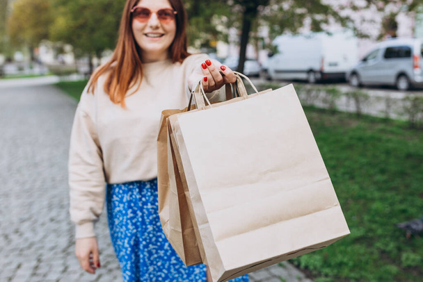 Happy young redhead woman holding shopping paper bags in hands, walking at city street, black friday. Urban lifestyle concept. Delivery carrying. - Foto, imagen