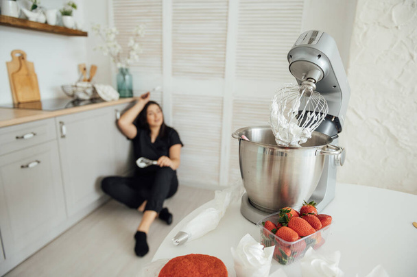 Woman cook sits on the floor against the background of a blender. Tired of a lot of orders - Photo, Image