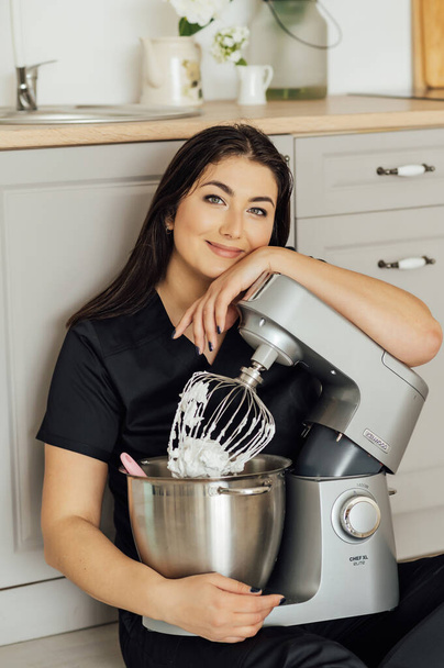 A woman cook sits on the floor and holds a professional mixer next to her. High quality blender for professionals - 写真・画像