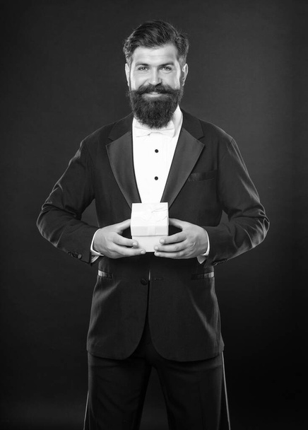 smiling man in tuxedo bow tie formalwear on black background with gift box. boxing day. - 写真・画像