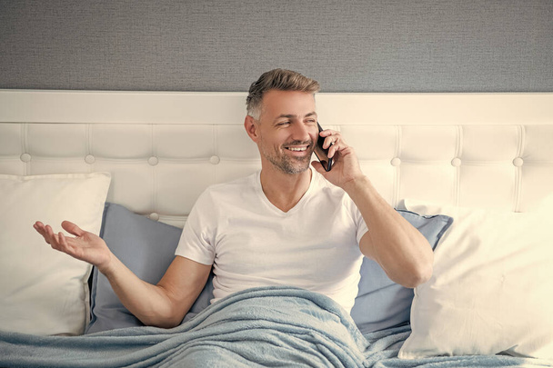 positive mature man in bed speaking on phone. - Fotó, kép