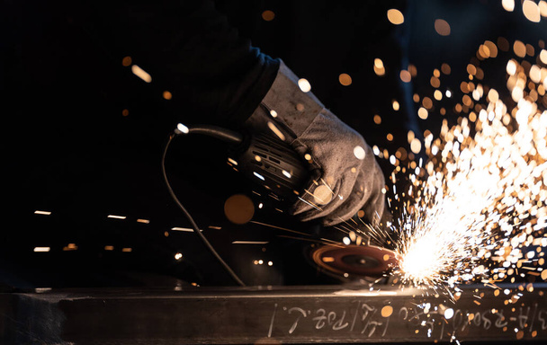 Man working on iron with grinder. Man at work. Sparkles and fire from grinder cutting. Grinder. Worker. - 写真・画像