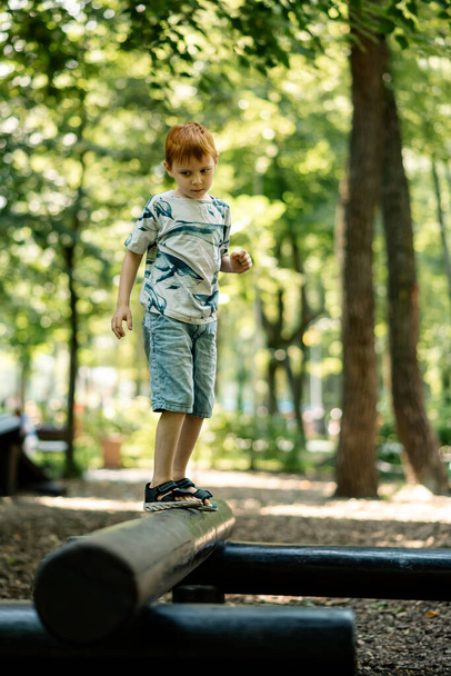 A young boy walks on a log at the playground. Active summer vacation. - Foto, Imagem