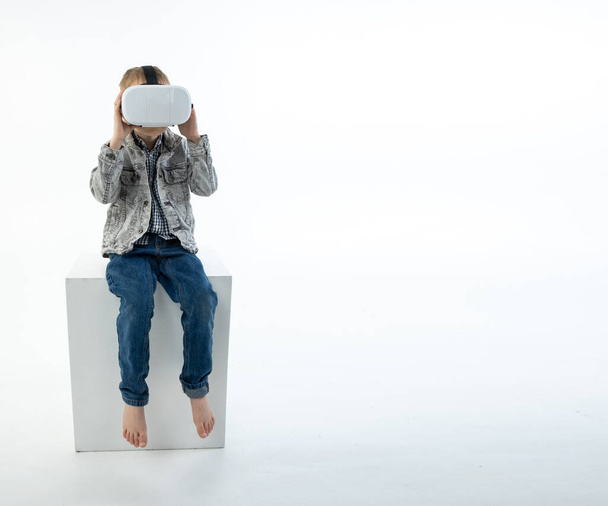 Young boy with virtual reality glasses on a white background. The child plays, looks, has fun with 3D glasses. - 写真・画像