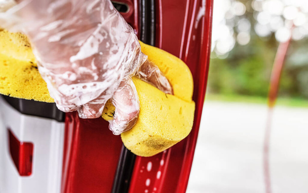 Young woman cleaning part of car door, closeup detail on hand in glove holding yellow sponge - Foto, immagini