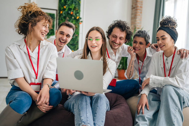 Eine Gruppe männlicher und weiblicher Berufstätiger in weißen Hemden sitzt zusammen mit einer jungen Frau, die einen Laptop in der Hand hält, und anderen, die ein Projekt glücklich betrachten und glücklich lächeln, arbeiten zusammen. - Foto, Bild
