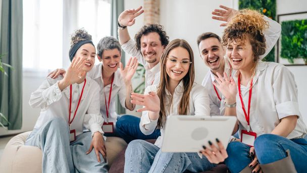 Skupina mužských a ženských profesionálů v bílých košilích mají videohovor na digitálním tabletu mladá žena drží zařízení všichni ostatní mávající šťastně se usmívat užijte si úspěšné virtuální setkání - Fotografie, Obrázek