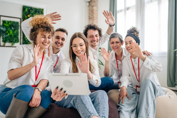A group of male and female professionals wearing white shirts are have a video call on a digital tablet young woman hold the device everyone else waving smiling happy enjoy successful virtual meeting - Photo, Image