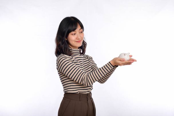 Portrait of young Asian woman holding white piggy bank isolated on white background, Financial and bank saving money concept - Zdjęcie, obraz
