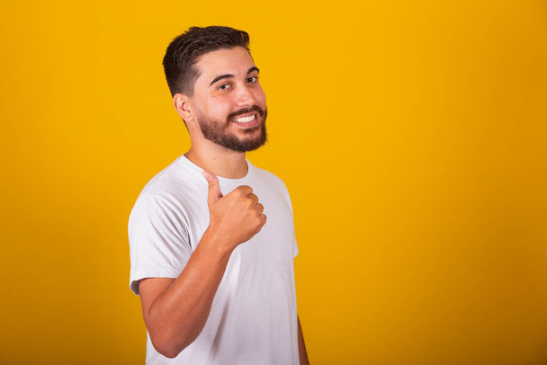 Brazilian Latin American man with thumb up, symbol of positive, approving, approved, cool, positivity, yellow background, space for text or advertisement - Foto, imagen