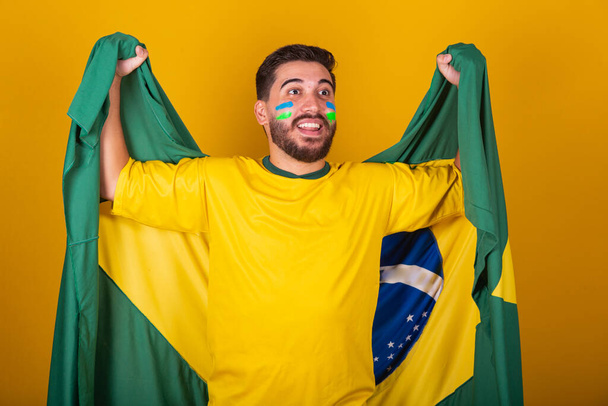 Brazilian man, latin american, cheering for brazil, in world cup 2022, Patriot, nationalist, Vibrating brazil flag, cheering and jumping, symbol of happiness, joy and celebration, with brazil flag - Foto, immagini