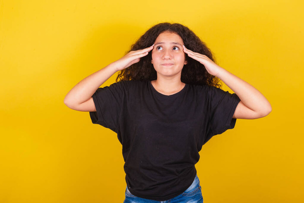 Brazilian, Latin American girl, for afro hair, yellow background, with hand on forehead and head, expression of doubt, forgetfulness, vixi, questioning, regret - Photo, Image