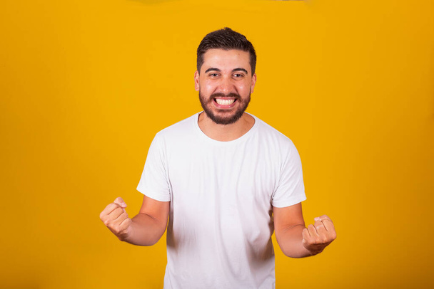 Brazilian Latin American man, with arms celebrating, Screaming with happiness, like a winner, joyful, happy, confident. yellow background - 写真・画像