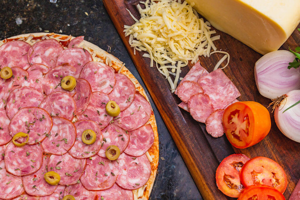 Pre-baked pepperoni pizza with fresh pizza ingredients on wooden board. - Fotó, kép