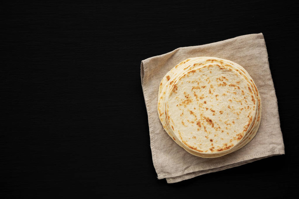 Stack of Whole Wheat Flour Tortillas on a black background, top view. Flat lay, overhead, from above. Copy space. - Φωτογραφία, εικόνα