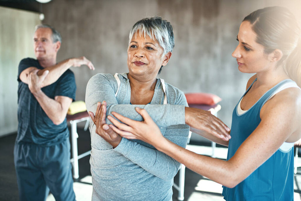 Stretching, physiotherapy and old woman with personal trainer for fitness, wellness or rehabilitation. Health, workout or retirement with senior patient and female trainer in gym for warm up training. - Photo, Image