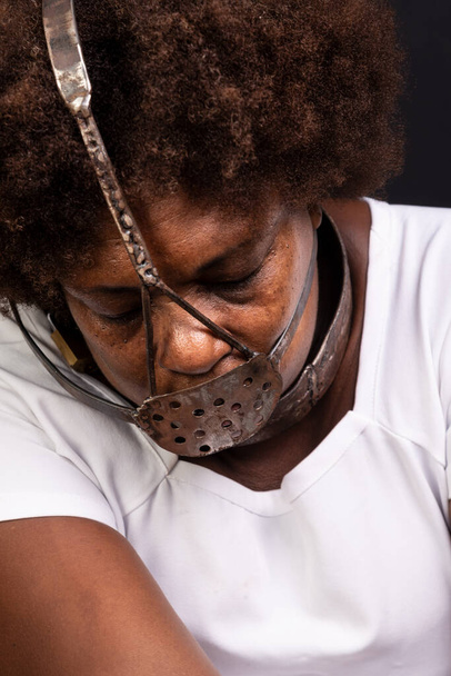 Черная женщина в цепях с железной маской на лице, представляющая рабыню Анастасию. Боль и страдания, пытки. На чёрном фоне. - Фото, изображение