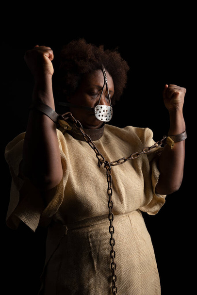 Portrét černošky s železnou maskou na tváři, která znázorňuje bolest otrokyně Anastacie. Izolováno na černém pozadí - Fotografie, Obrázek
