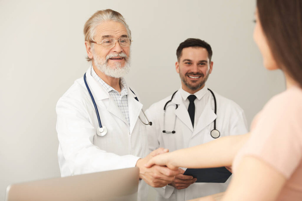 Happy senior doctor shaking hands with patient in clinic - Foto, Imagen