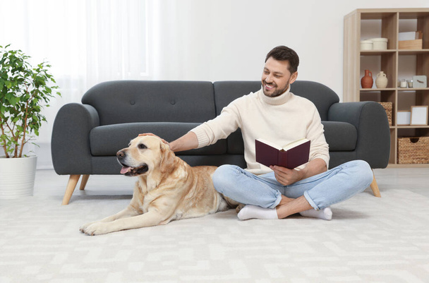 Man reading book on floor near his cute Labrador Retriever at home - Foto, Bild