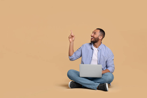 Smiling young man with laptop on beige background, space for text - Fotó, kép