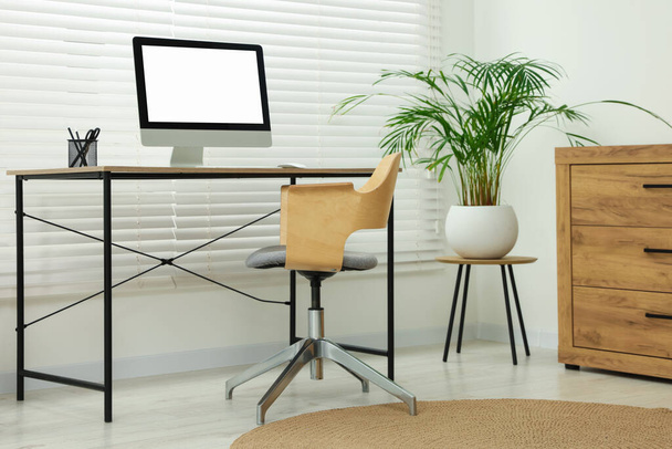 Stylish office interior with comfortable chair, desk, computer and houseplant - Fotoğraf, Görsel
