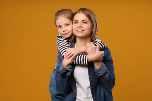 Little daughter hugging her mom on orange background. Happy Mother's Day - Photo, Image