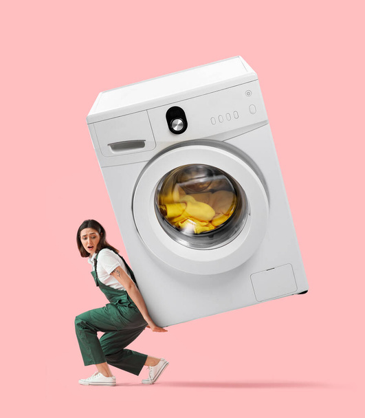 Fontanero mujer preocupado con lavadora grande sobre fondo rosa - Foto, Imagen
