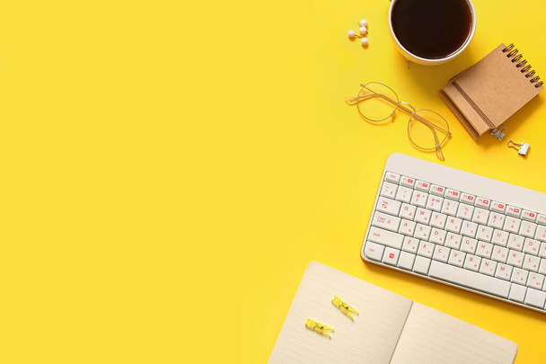 Composición con taza de café, teclado, vasos y cuaderno sobre fondo amarillo - Foto, Imagen
