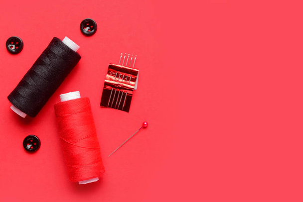 Komposition mit Garnspulen, Knöpfen und Nadeln auf rotem Hintergrund - Foto, Bild