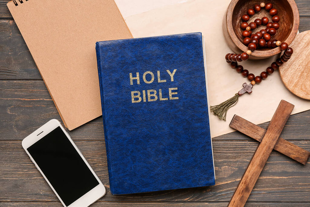 Holy Bible with prayer beads, mobile phone, notebook and cross on wooden background - Фото, изображение