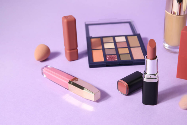Lippenstifte und verschiedene Kosmetika auf fliederfarbenem Hintergrund - Foto, Bild