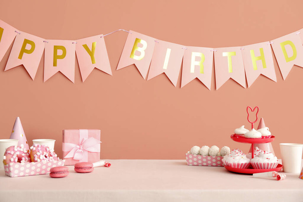 Sweets on white table and happy birthday paper garlands on dark beige wall - Photo, image
