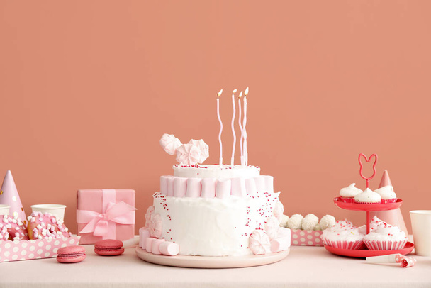 Tort urodzinowy ze świeczkami i słodyczami na białym stole przy ciemnobeżowej ścianie - Zdjęcie, obraz