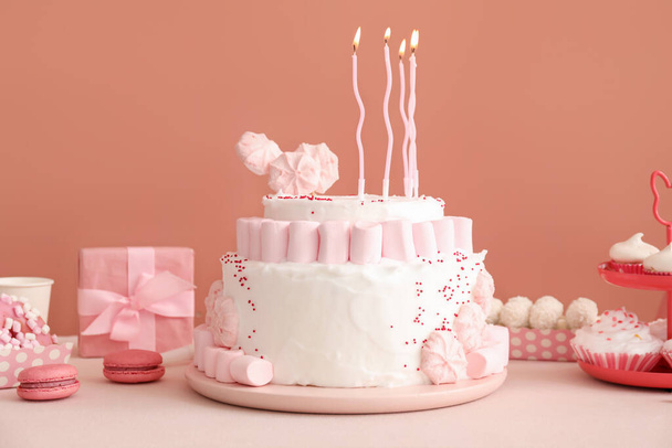 Торт на день рождения со свечами и сладостями на белом столе возле тёмно-бежевой стены - Фото, изображение