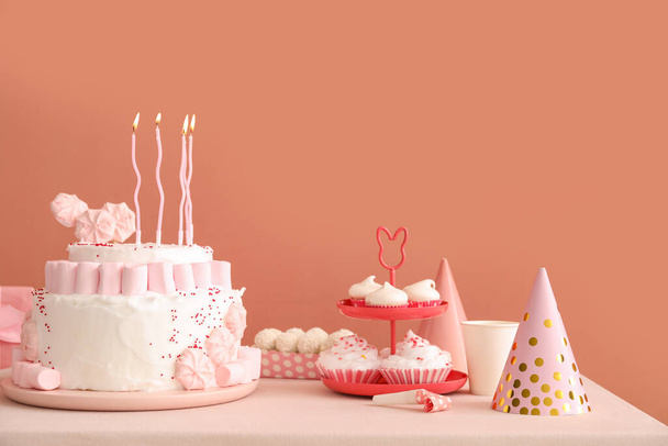 Koyu bej duvarın yanındaki beyaz masada mumlar ve şekerler olan doğum günü pastası. - Fotoğraf, Görsel
