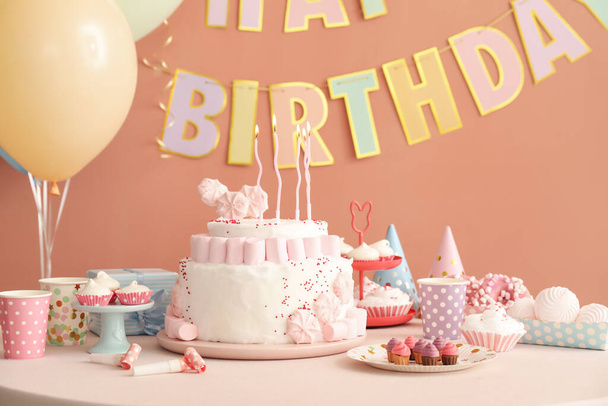 濃いベージュの壁の近くの白いテーブルの上にキャンドルやお菓子と誕生日ケーキ - 写真・画像
