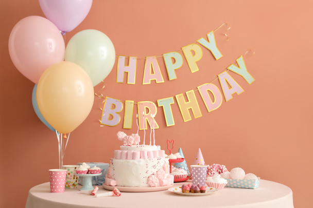 Verjaardagstaart met kaarsen en snoepjes op witte tafel bij donker beige muur - Foto, afbeelding