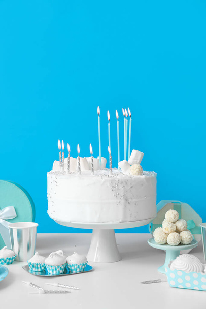 Birthday cake with candles and sweets on white table near blue wall - Photo, Image