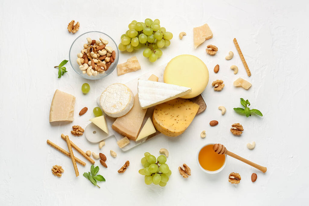 Board with different types of tasty cheese, grapes, nuts and honey on light background - Fotó, kép