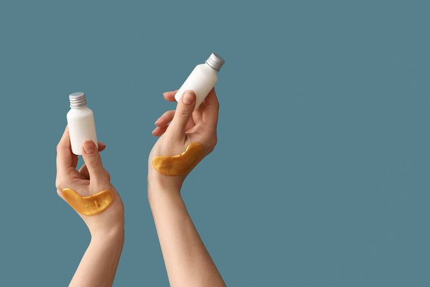 Hands with bottles of cosmetic product and under-eye patches on blue background - Photo, Image