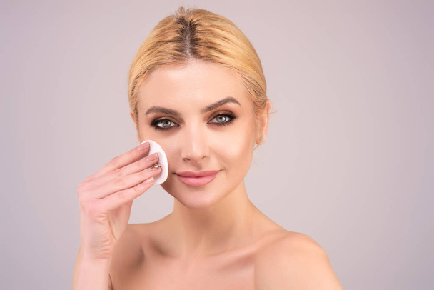 Woman removing makeup with cotton pad near face. Skin care. Girl with cotton pad, studio isolated background. Moisturizing skin by special face cream before applying foundation - Foto, Bild