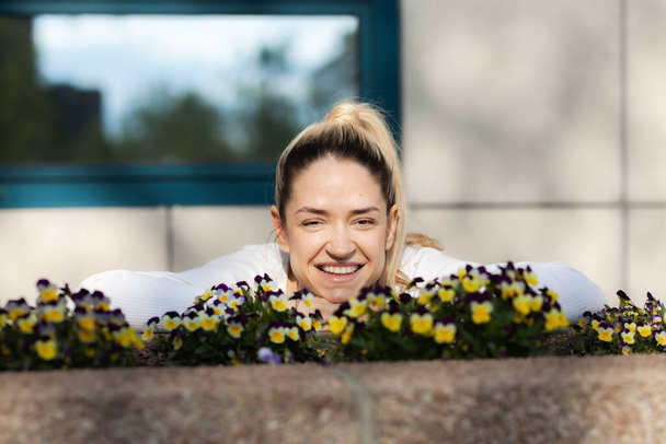 Outdoor portrait of a beautiful city girl laughing infront of flowers with urban background. - Фото, зображення