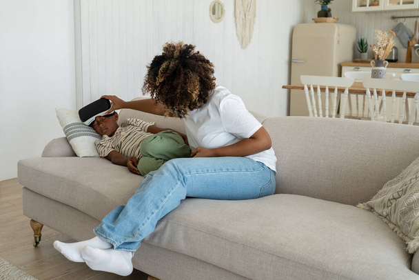 Äiti ottaa pois virtuaalitodellisuus kypärä addiktoitunut teini poika istuu sohvalla kotona. Poika nukkuu VR suojalasit pelaa pelejä katsomassa elokuvaa. Yli käyttämällä vempaimia, pelaamista vr riippuvuus, uupunut käsite. - Valokuva, kuva