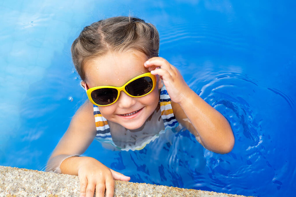 Πορτρέτο ενός ευτυχισμένου παιδιού με γυαλιά ηλίου στο νερό - Φωτογραφία, εικόνα