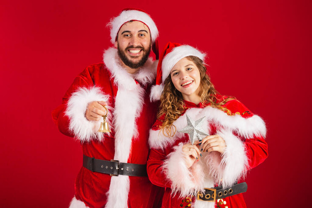 Brazilian couple, dressed in Christmas clothes, Santa Claus, holding Christmas decorations, star, bell. - Foto, imagen
