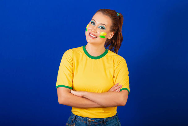 fehér nő, vöröshajú, brazil futball rajongó, brazil, kék háttér, karok keresztbe optimista - Fotó, kép