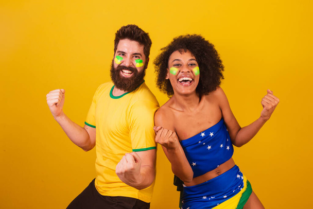 couple of brazilian soccer fans, dressed in the colors of brazil, black woman, caucasian man. screaming goal - Foto, Imagen
