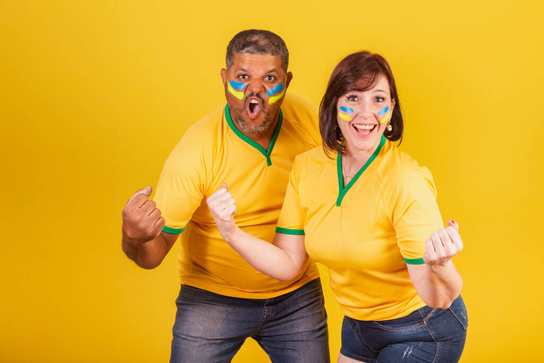 Couple, red-haired woman and black man, Brazilian soccer fans. celebrating. - 写真・画像